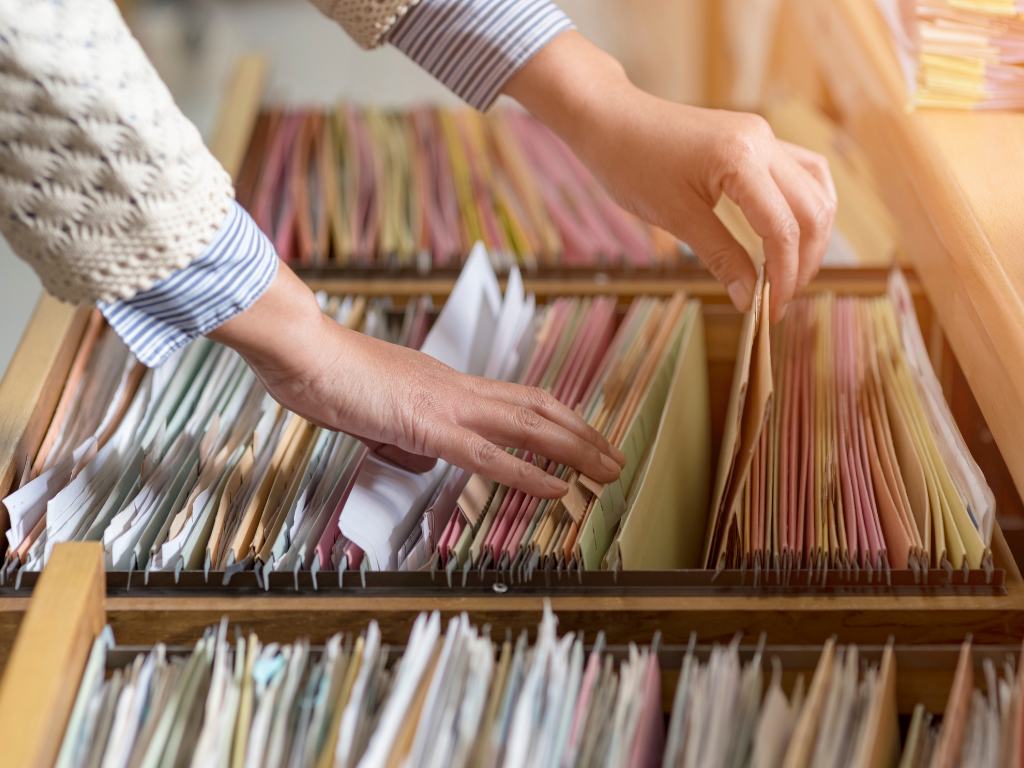 Woman's hands taking a file from an old-school filing cabinet