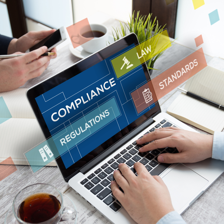 Hands on a laptop keyboard. The words compliance, law, regulations, and standards are superimposed over the screen